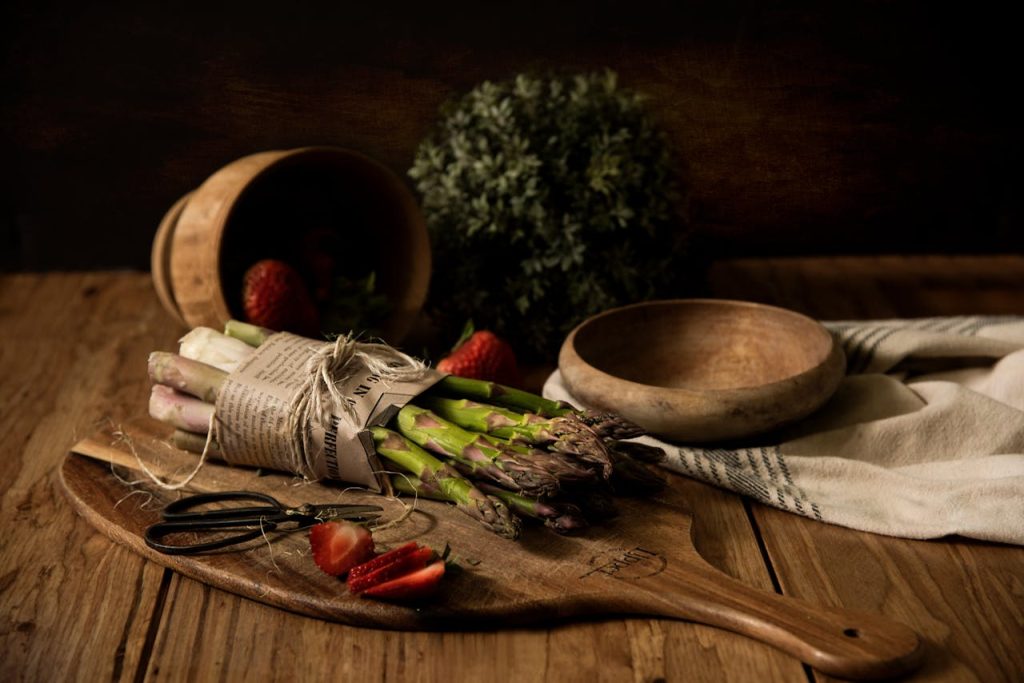 A rustic arrangement of asparagus and strawberries on a wooden board, captured in warm tones.